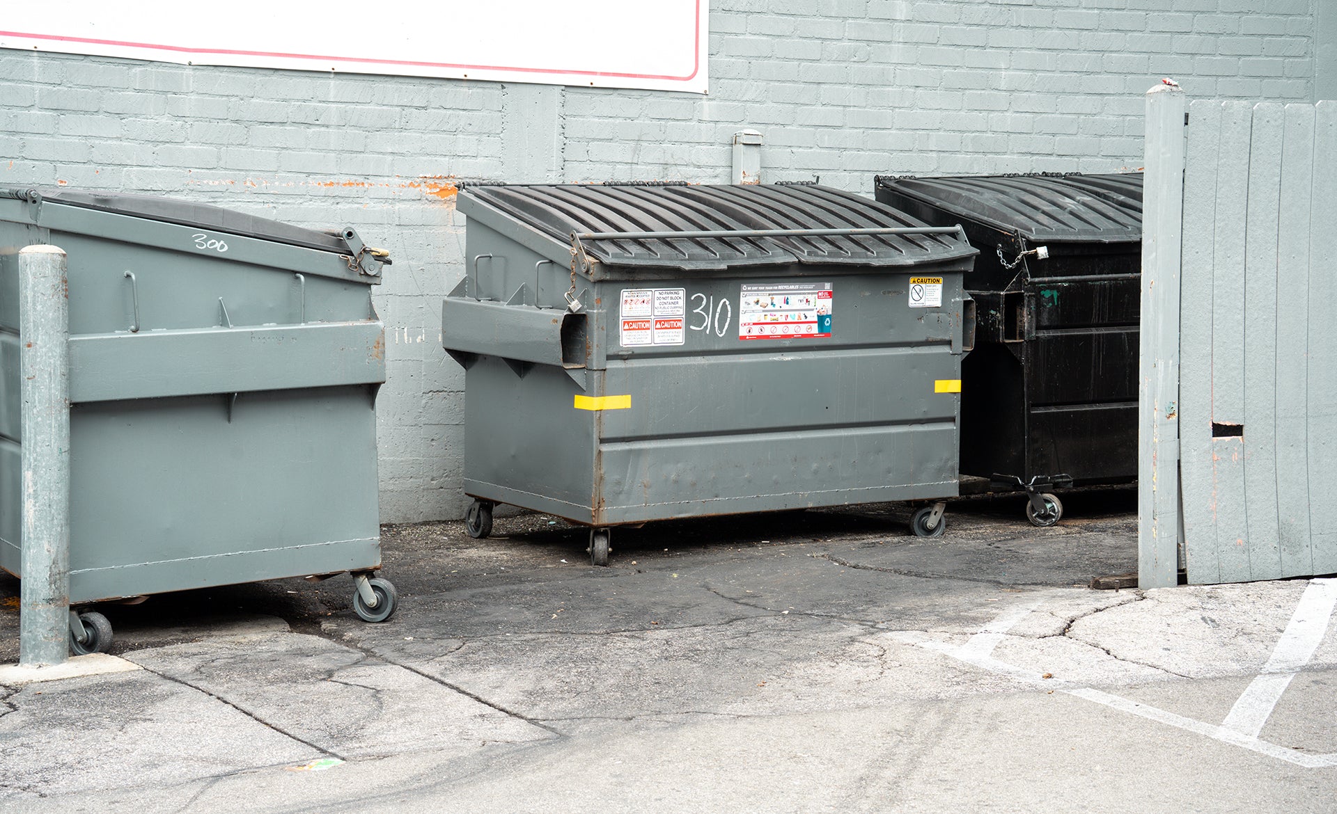 Commercial front-load dumpsters behind a business, serviced by Enviro Can Clean